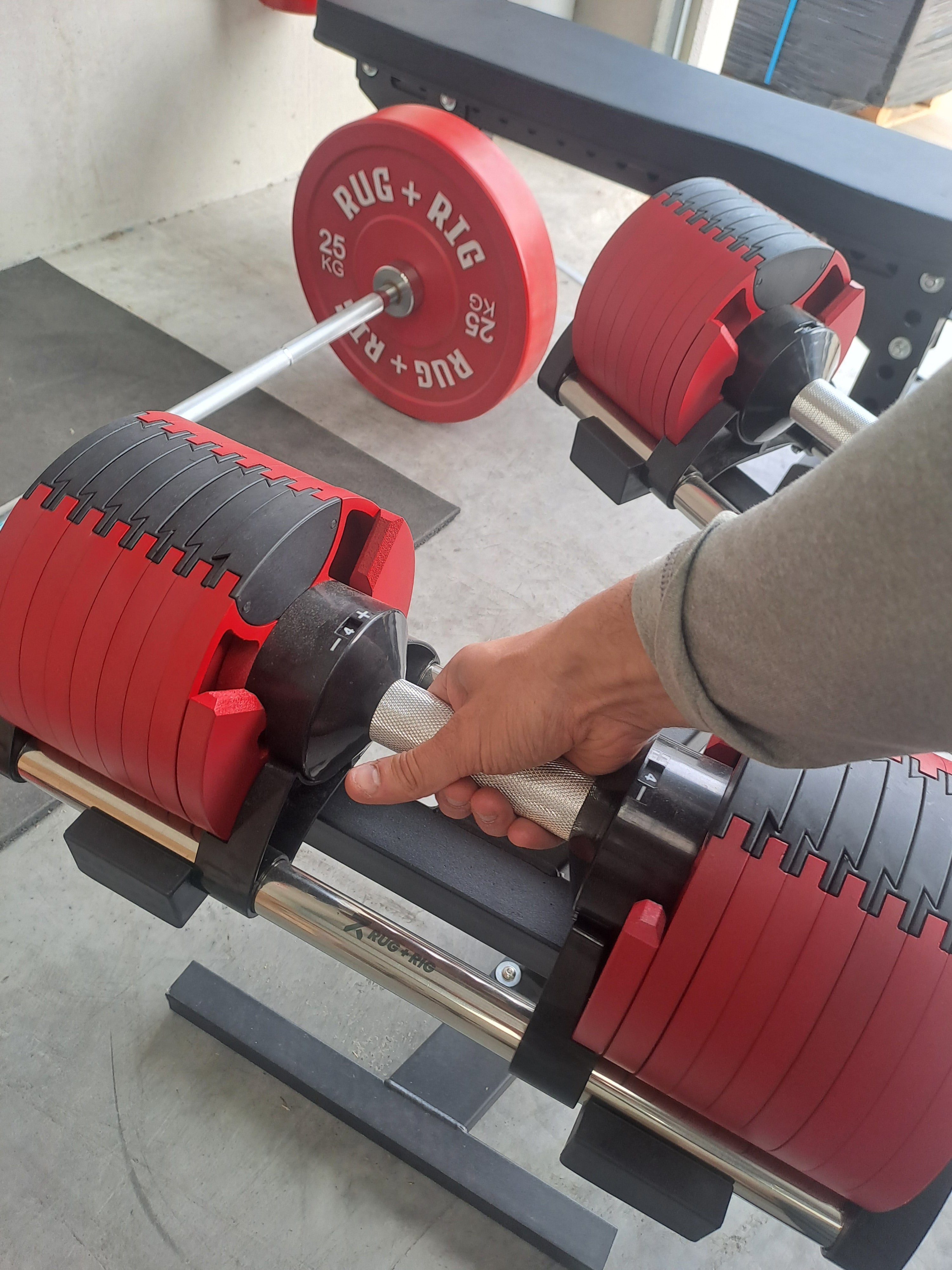 Person adjusting red weight plates on a adjustable dumbbell handle